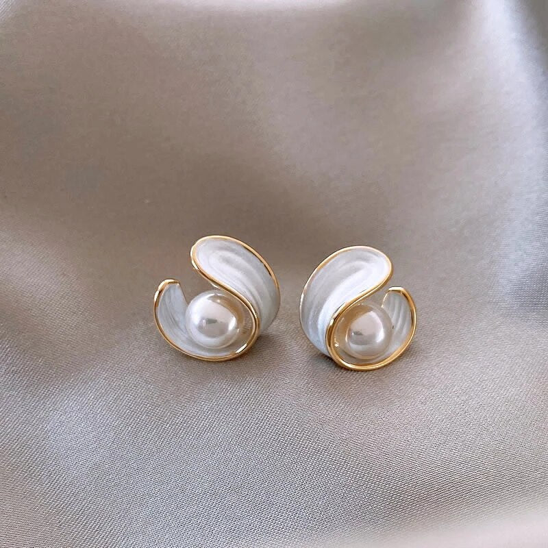 Elegant gold and pearl earrings on satin fabric, featuring a swirl design with white enamel accents. Luxurious jewelry, perfect for formal occasions.