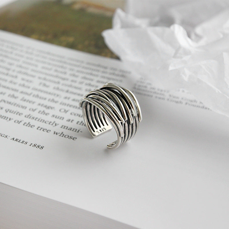 Silver adjustable ring with layered design on open book page, showcasing elegant craftsmanship. Perfect for fashion jewelry enthusiasts.