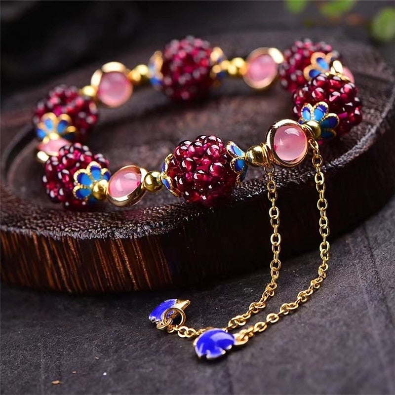 Elegant gold bracelet with red gemstone clusters, pink cabochons, and blue floral accents on a wooden surface. Luxurious jewelry accessory.