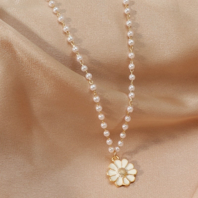 Elegant pearl necklace with daisy pendant on beige satin background, showcasing luxury jewelry, floral design, and fashion accessories.