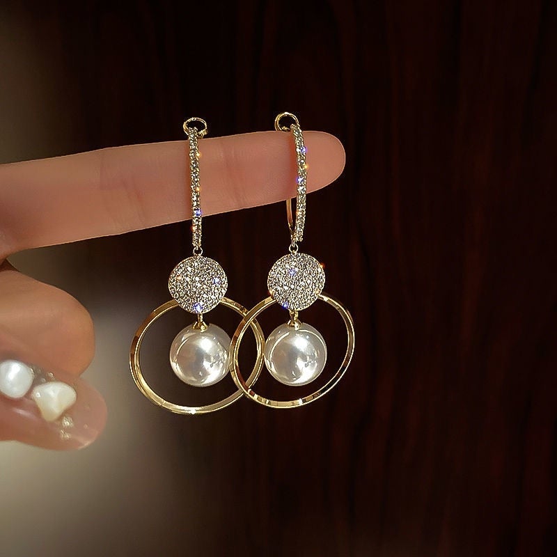 Elegant gold drop earrings with sparkling crystals and pearl accents, featuring circular hoop design. Perfect for luxury fashion and jewelry enthusiasts.