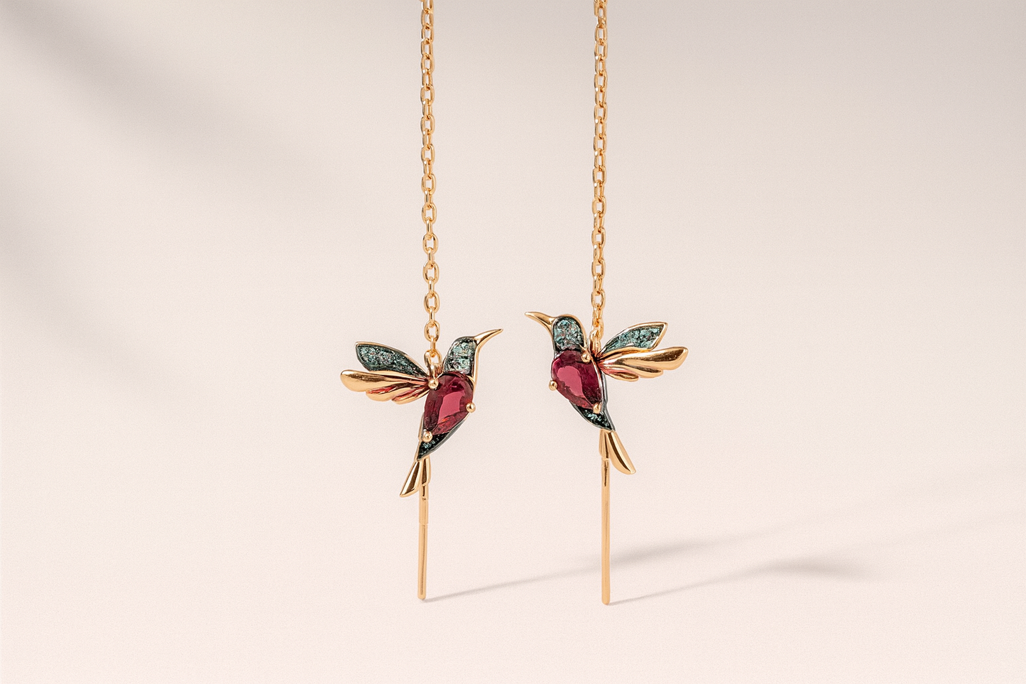 Gold hummingbird earrings with gemstones on a beige background