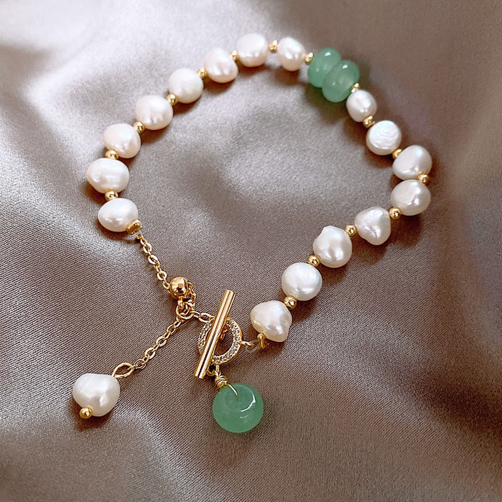 Elegant pearl bracelet with gold accents and green jade charm on satin fabric. Luxurious jewelry, freshwater pearls, toggle clasp, fashion accessory.