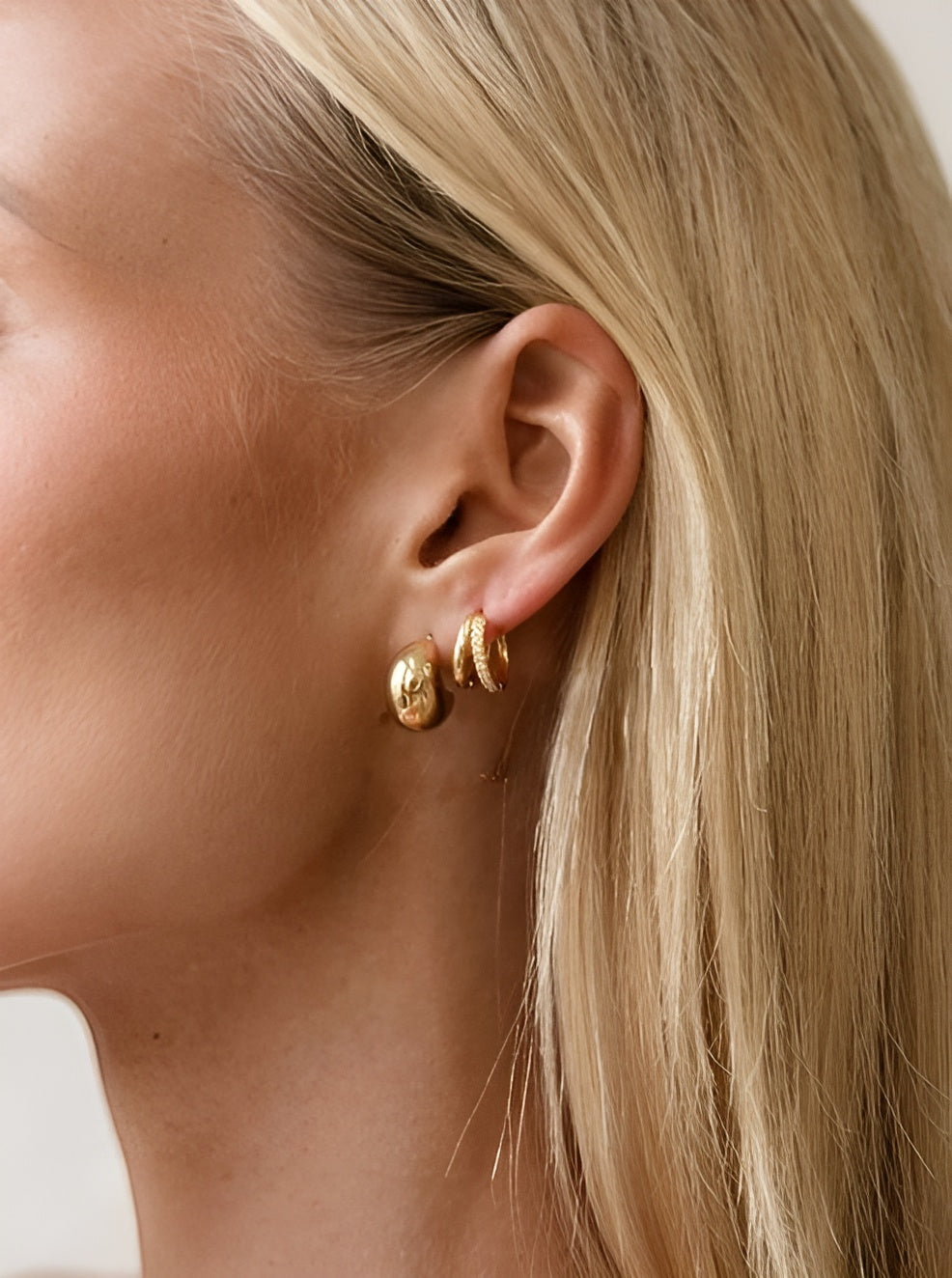 Close-up of a person wearing gold hoop earrings with a neutral background