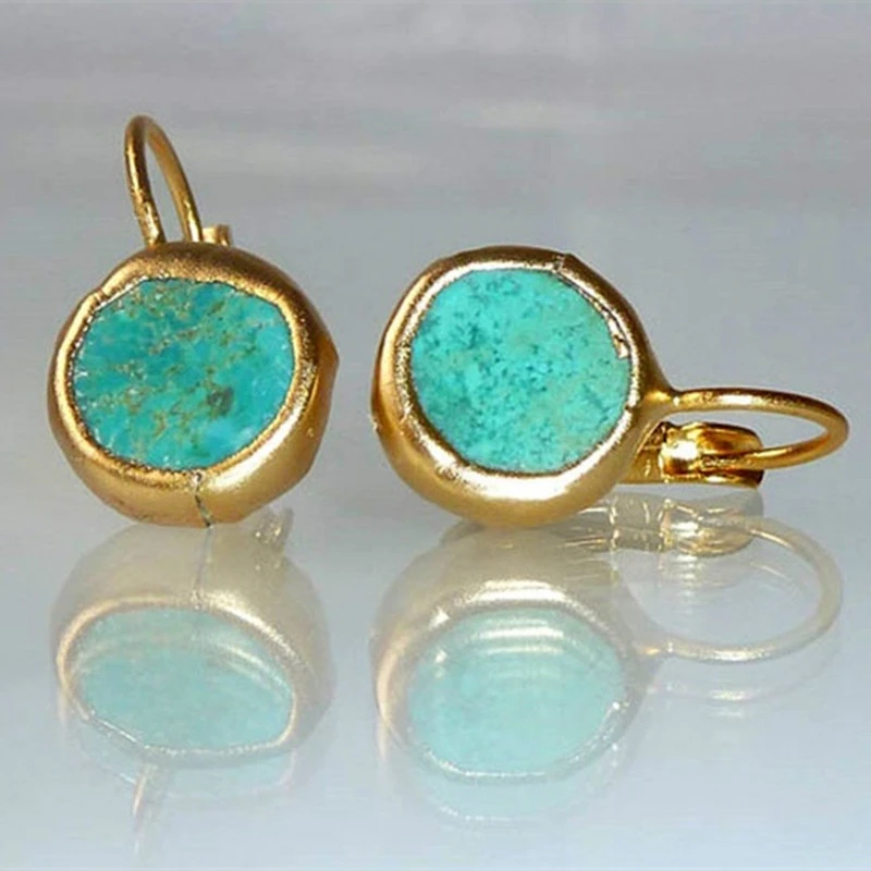 Gold turquoise earrings with round stones, reflecting on a glossy surface. Elegant jewelry, perfect for fashion accessories and gemstone enthusiasts.