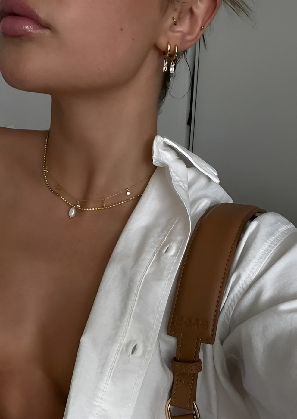 Close-up of a person wearing a gold necklace with a pearl pendant and earrings.