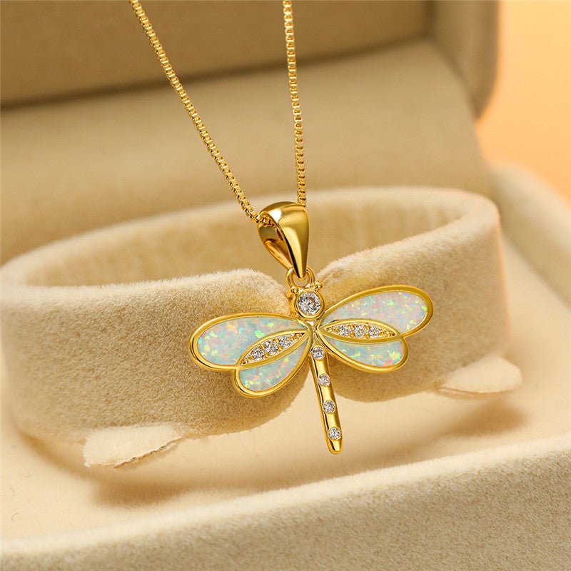 Gold dragonfly pendant necklace with opal inlay and diamond accents, displayed in a beige jewelry box. Elegant and luxurious jewelry piece.