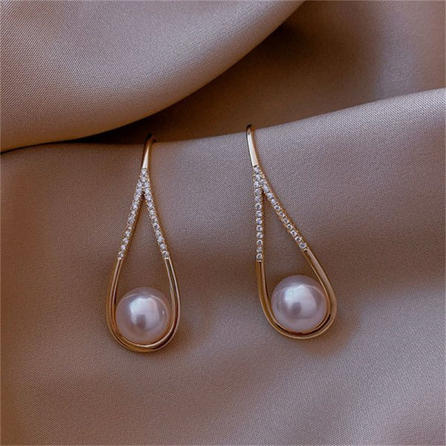 Elegant gold drop earrings with pearls and diamond accents on a satin fabric background. Luxurious jewelry, perfect for weddings and special occasions.
