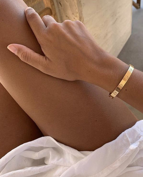 Hand wearing a gold bracelet on a blurred background