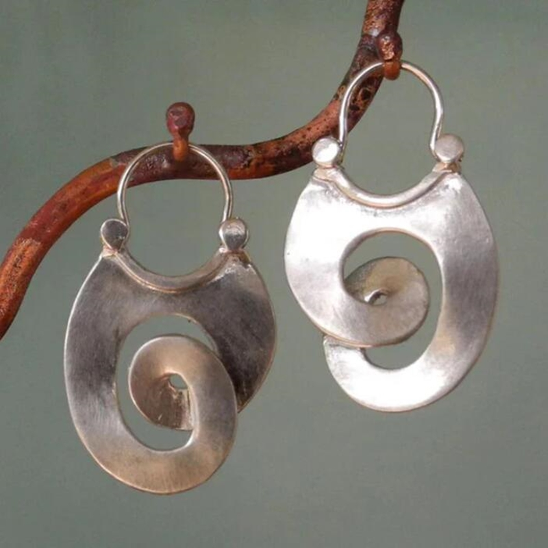 Silver spiral earrings hanging on a branch with a green background