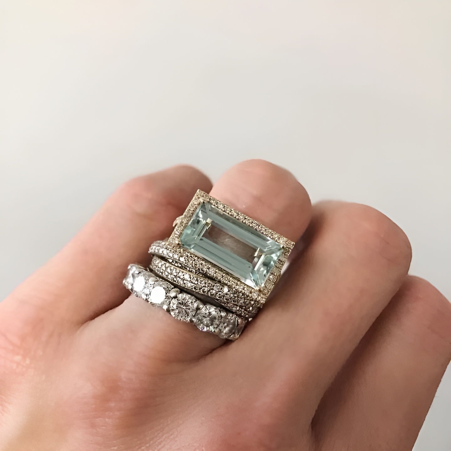 Hand wearing a stack of rings with a prominent gemstone on a plain background