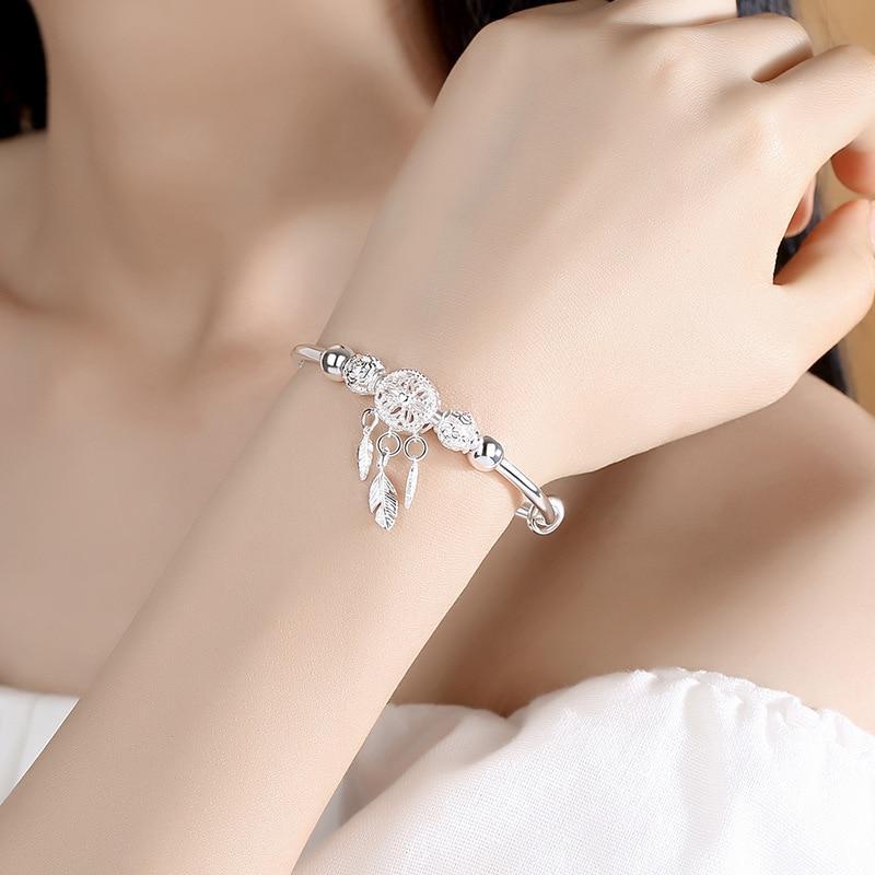 Silver charm bracelet with feather and dreamcatcher pendants on woman's wrist, elegant jewelry accessory, perfect for fashion and style enthusiasts.