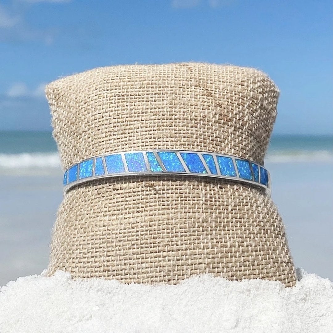 Blue opal inlay bracelet on burlap display at beach, showcasing vibrant ocean colors and silver accents, perfect for coastal jewelry fashion.