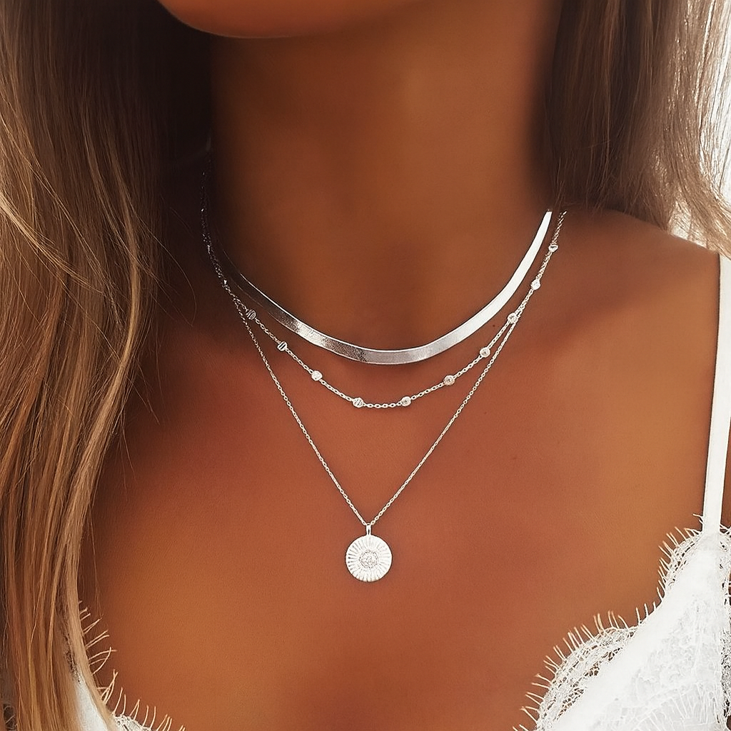 Close-up of a woman wearing layered silver necklaces, featuring a sunburst pendant, over a white lace top. Fashion jewelry, elegant style.