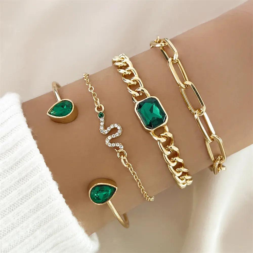 Gold and emerald bracelet set on wrist, featuring snake design, chain links, and teardrop gems. Elegant jewelry for fashion and style enthusiasts.