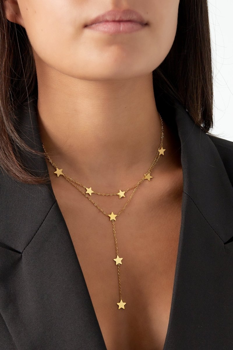 Gold star necklace worn by a person against a neutral background