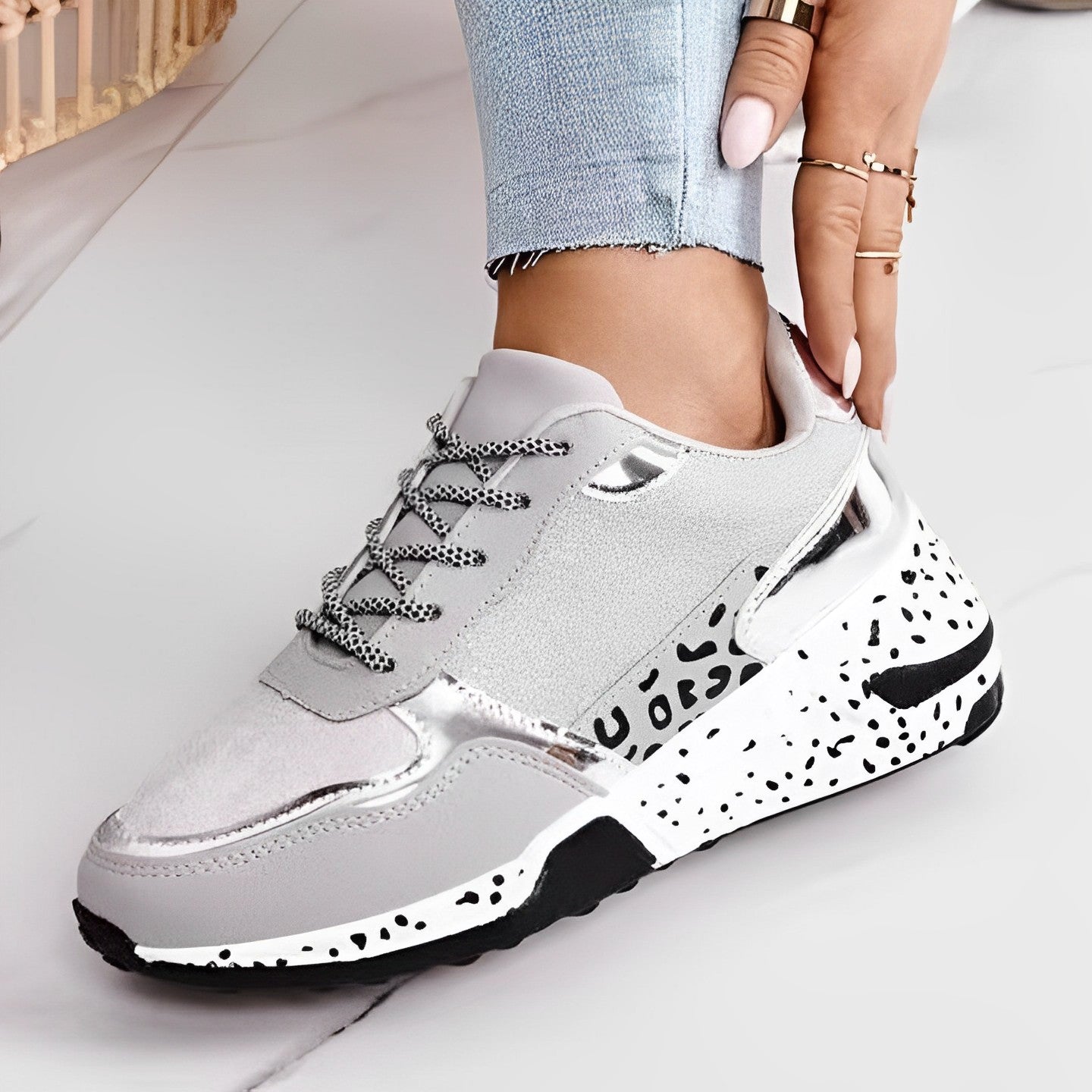 Gray sneaker with black and white speckled sole worn by a person on a light background