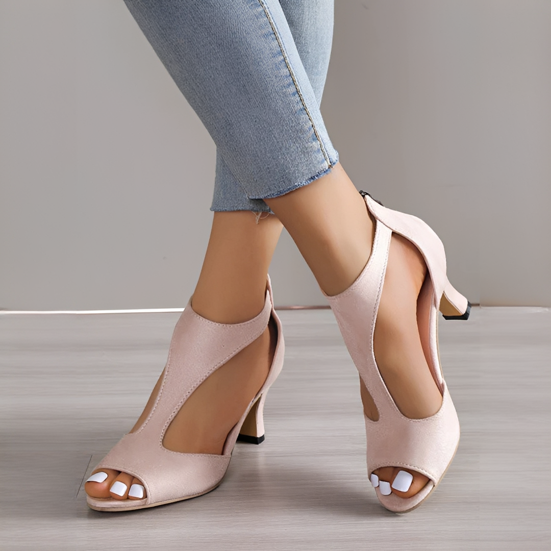 Beige high-heeled shoes worn with light blue jeans on a neutral background