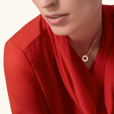 Woman wearing a gold circle pendant necklace and a red blouse, showcasing elegant jewelry fashion.