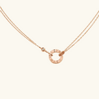 Rose gold necklace with circular pendant featuring engraved letters, delicate double chain, and small diamond accent. Elegant jewelry accessory.