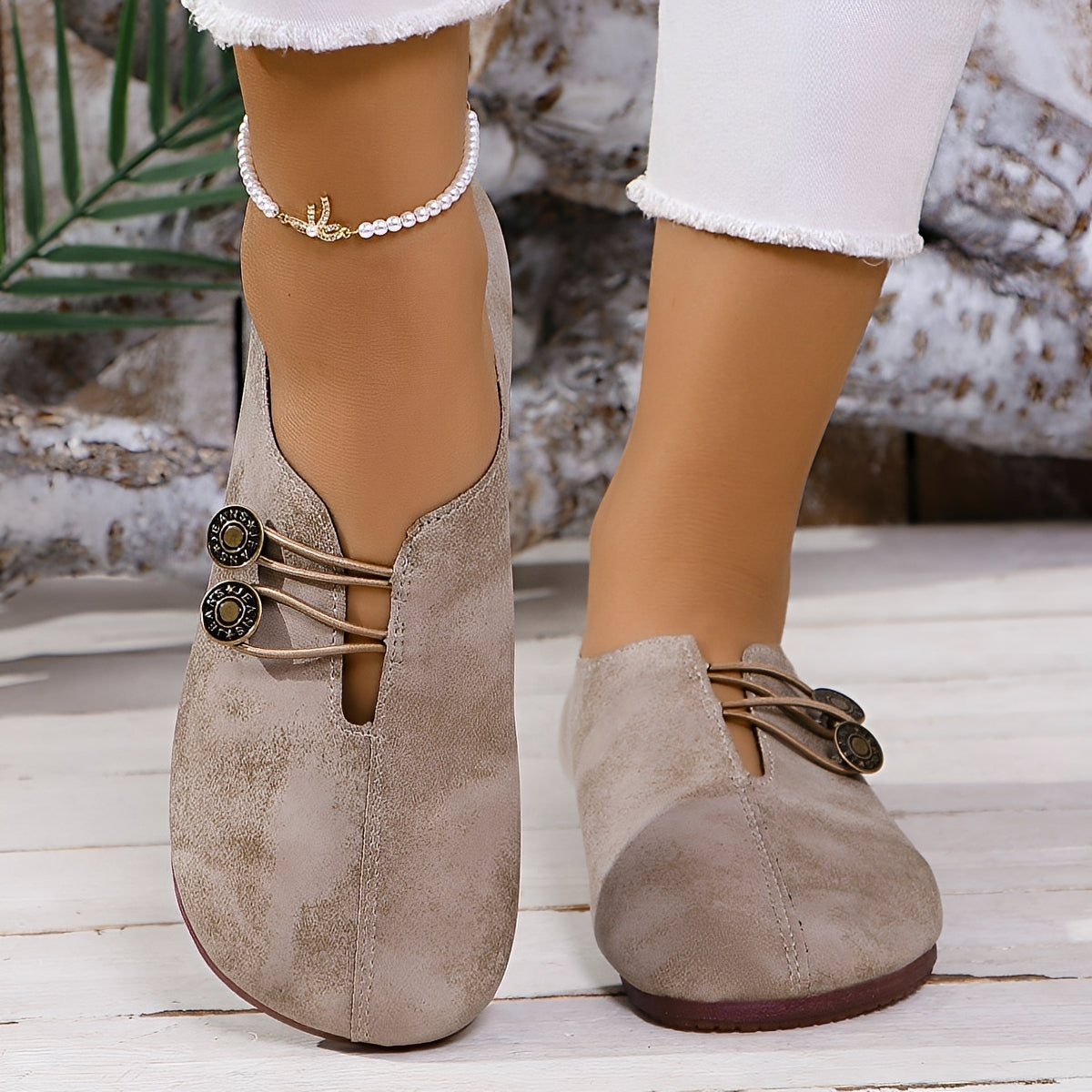Beige suede shoes with brown soles worn by a person on a wooden floor.