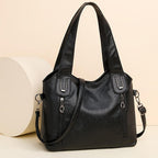 Black handbag with multiple zippers on a beige background