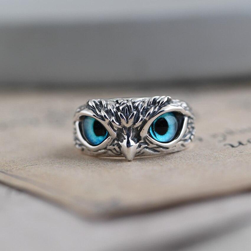 Silver owl ring with intricate detailing and striking blue gemstone eyes, resting on a textured surface. Unique jewelry design, animal-inspired accessory.