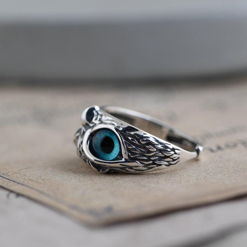 Silver ring with intricate feather design and blue eye gemstone, resting on vintage paper. Unique jewelry, boho style, artisan craftsmanship.