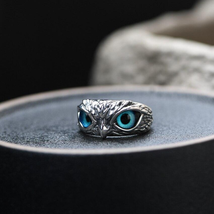 Silver owl ring with striking blue eyes, detailed craftsmanship, resting on a dark surface. Unique animal jewelry, nature-inspired accessory.