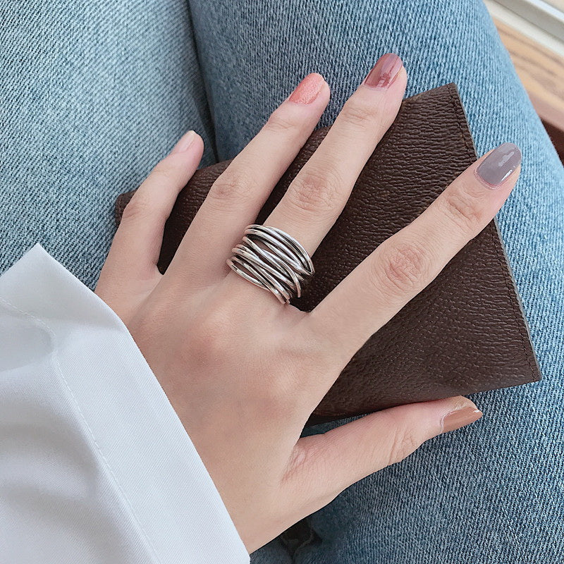 Hand wearing multiple silver stackable rings holding a brown leather wallet, showcasing trendy minimalist jewelry against blue denim jeans.