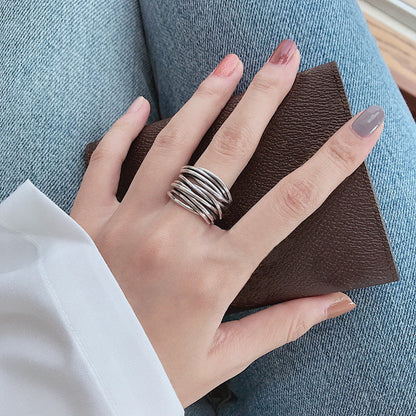 Hand wearing multiple silver stackable rings holding a brown leather wallet, showcasing trendy minimalist jewelry against blue denim jeans.