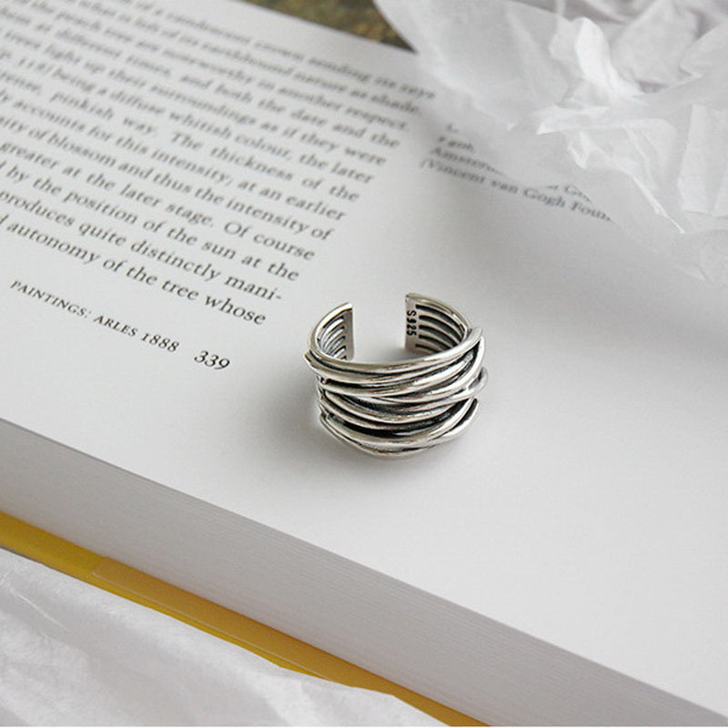 Silver adjustable ring with layered design on open book page, modern minimalist jewelry, stylish accessory for fashion-forward individuals.