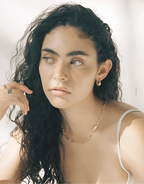 Woman with long, wavy hair wearing a gold necklace against a neutral background
