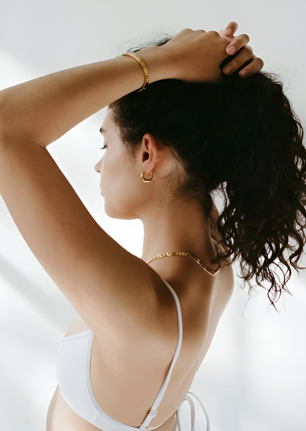 Woman wearing a white bikini with gold jewelry against a light background