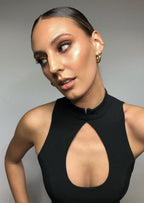 Woman in elegant black cutout dress with sleek hairstyle and gold hoop earrings, showcasing glowing makeup and highlighted cheekbones.