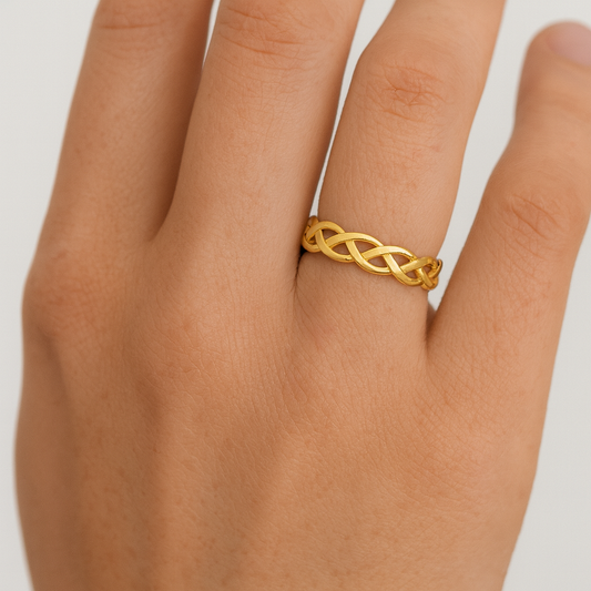 Gold braided ring on a person's finger against a white background