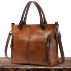 Brown leather handbag with multiple pockets and straps on a wooden surface.