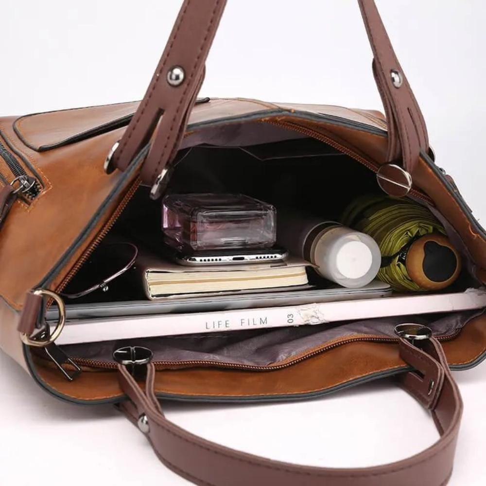 Brown leather handbag with its contents displayed on a white background