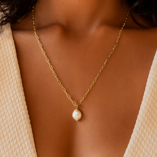 Gold chain necklace with a single pearl pendant on a woman's neck, wearing a textured beige top. Elegant jewelry, minimalist fashion accessory.