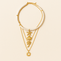Gold layered necklace with seashell, starfish, palm tree, and sun charms on a beige background. Boho beach jewelry, summer fashion accessory.