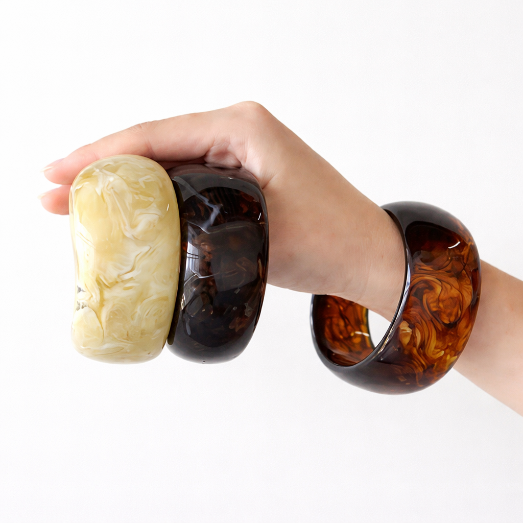 Hand holding three marbled resin bracelets on a white background