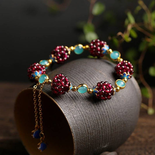 Elegant beaded bracelet with red and blue gemstones on a dark ceramic cup, featuring gold chain accents. Perfect for jewelry fashion enthusiasts.
