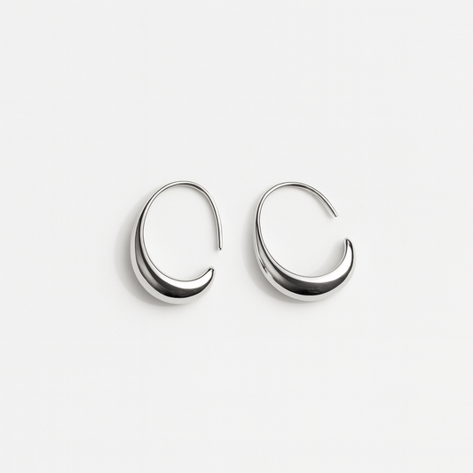 Silver crescent-shaped hoop earrings on white background, minimalist jewelry, modern fashion accessories, elegant design, women's earrings.