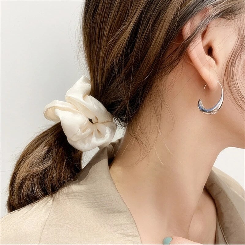 Woman with brown hair in a ponytail, wearing a white scrunchie and silver hoop earring, beige blazer; fashion accessories close-up.