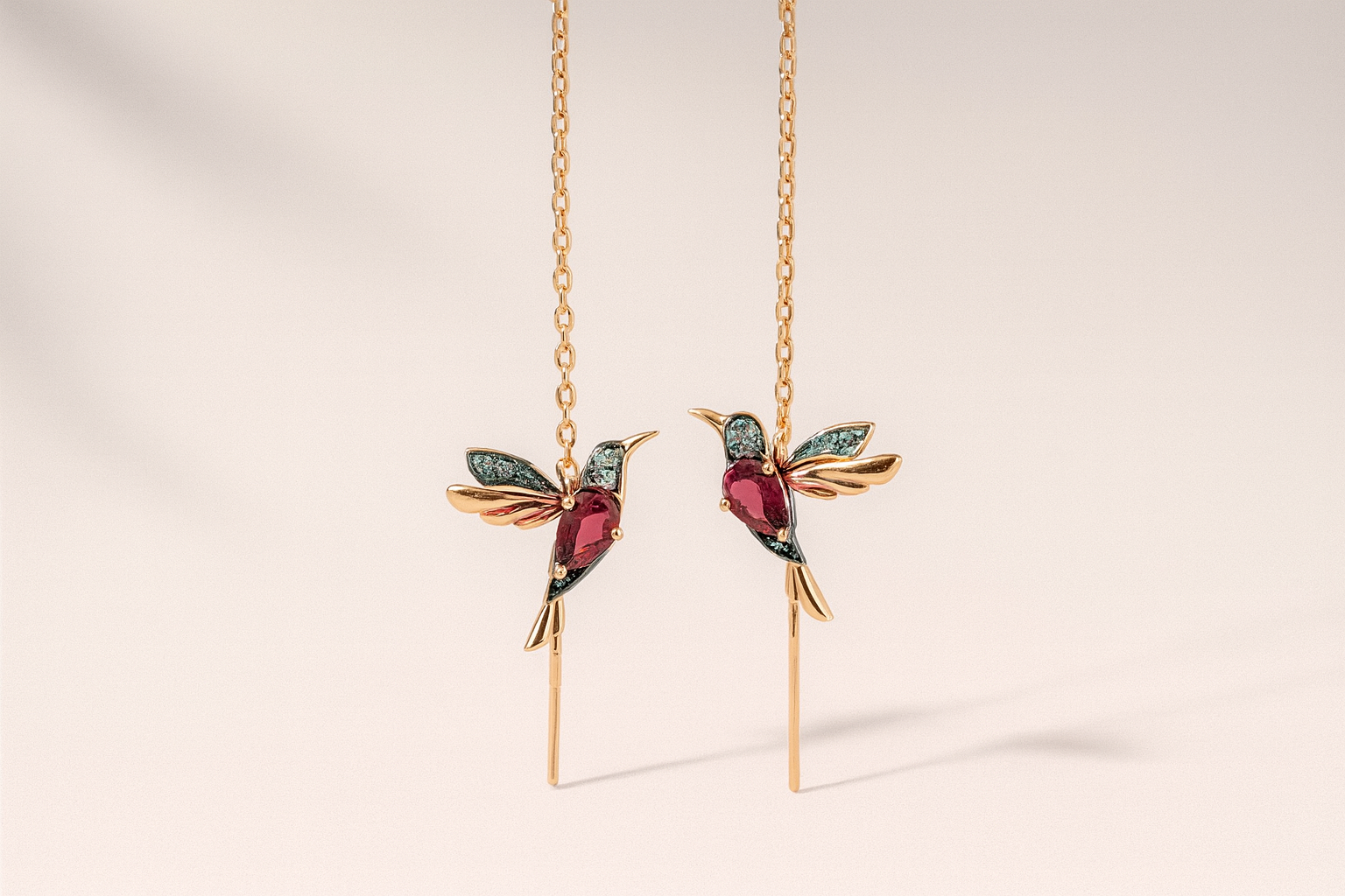 Gold hummingbird earrings with gemstones on a beige background