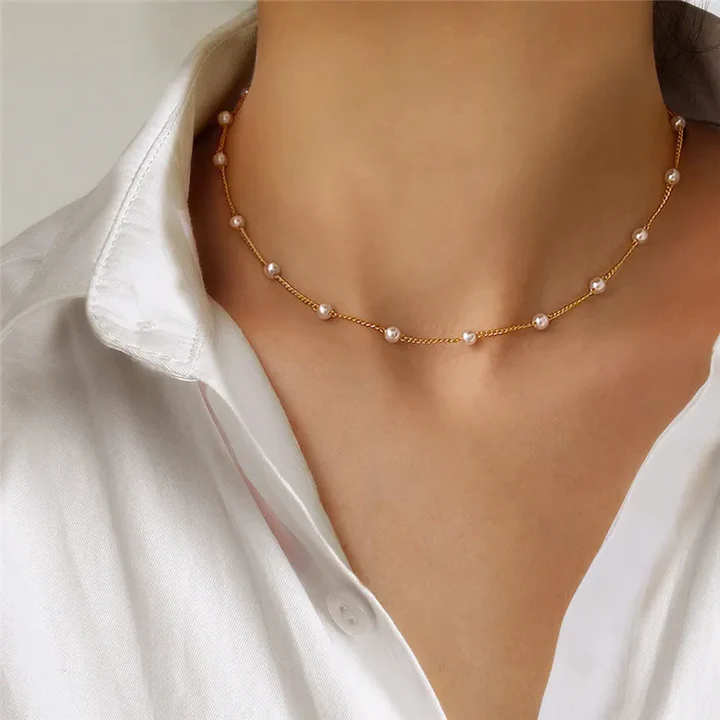 Gold chain necklace with pearls on a woman's neck, paired with a white collared shirt. Elegant jewelry, fashion accessory, minimalist style.
