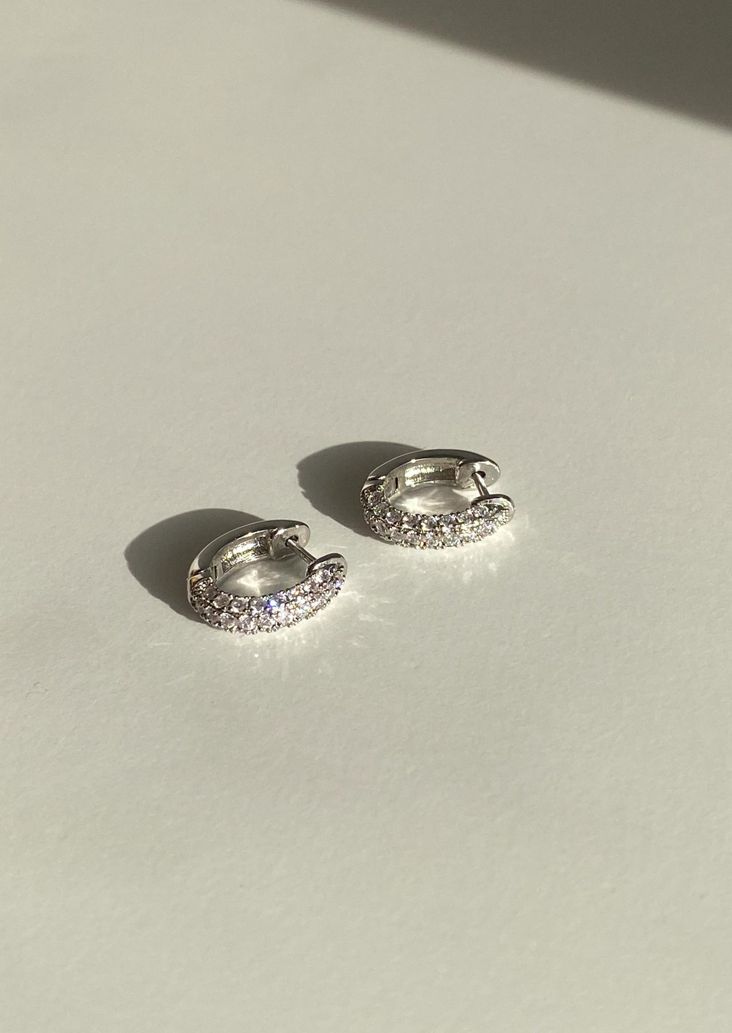 Pair of silver hoop earrings with clear stones on a light background