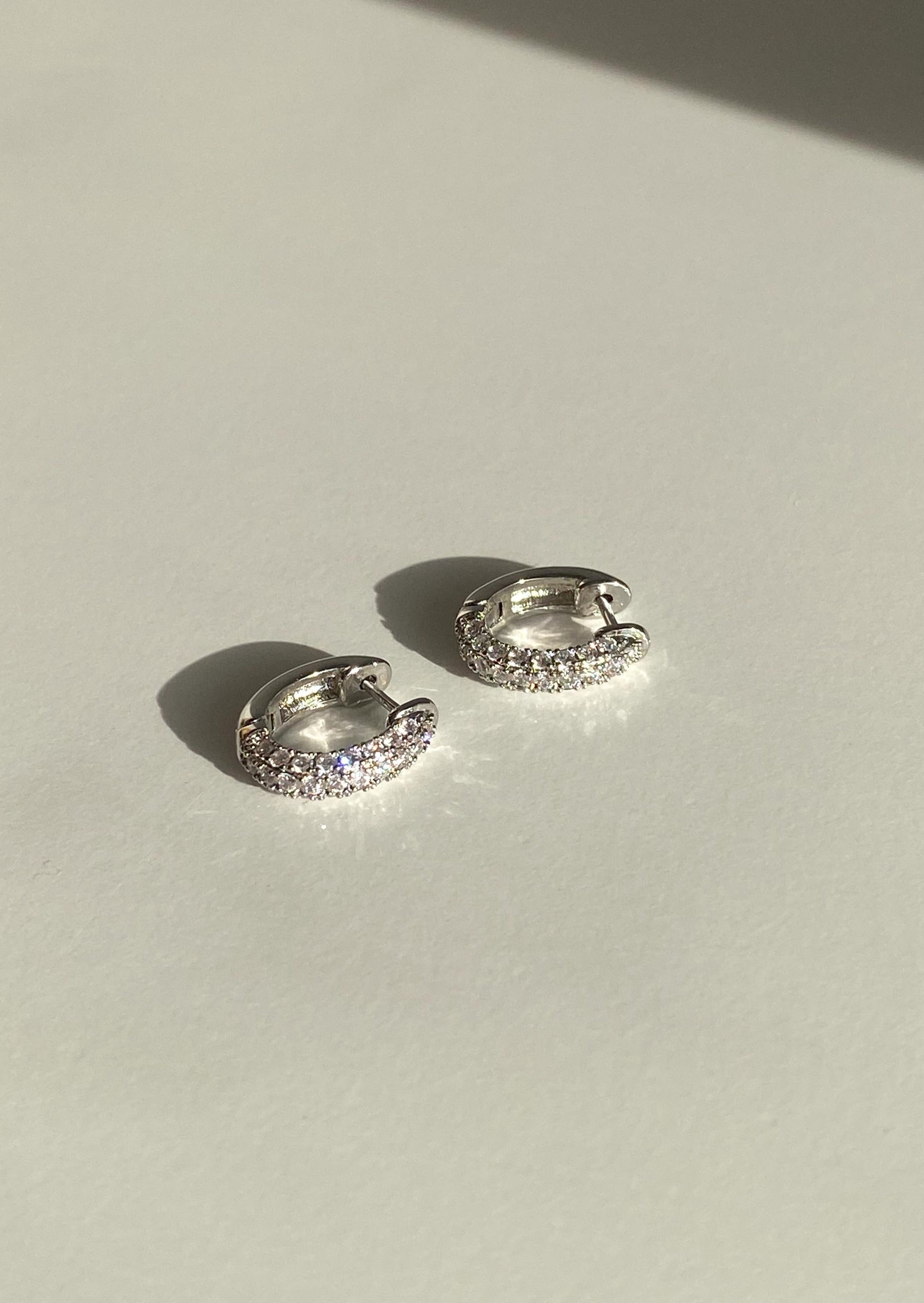 Pair of silver hoop earrings with clear stones on a light background