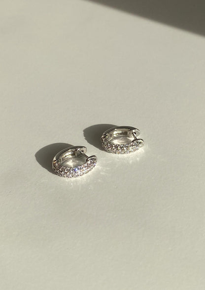 Pair of silver hoop earrings with clear stones on a light background