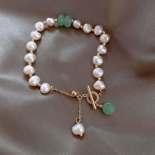 Elegant pearl bracelet with gold chain and toggle clasp, featuring green jade beads, displayed on luxurious satin fabric. Perfect for jewelry lovers.